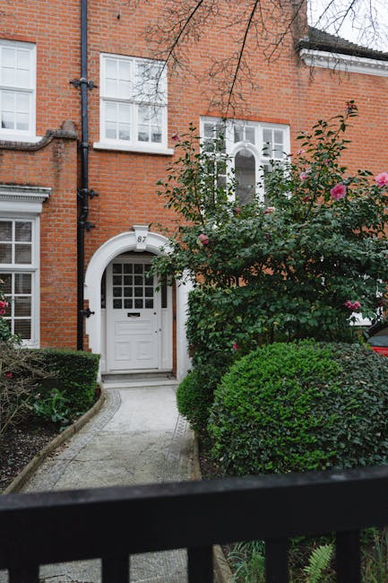 The image shows the entrance to a residential property featuring a classic black front door with intricate glass panel details. Surrounding the door is a decorative white stone arch with carved floral